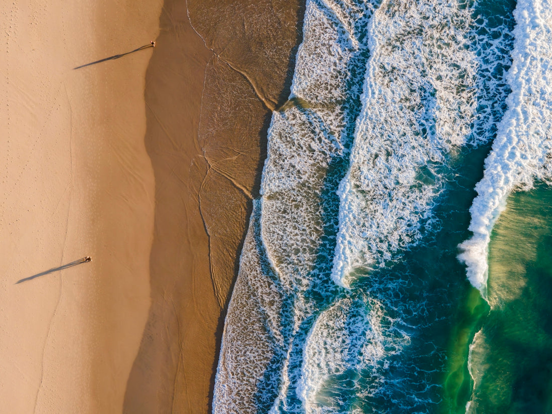 Waves crash on a sandy beach from above.